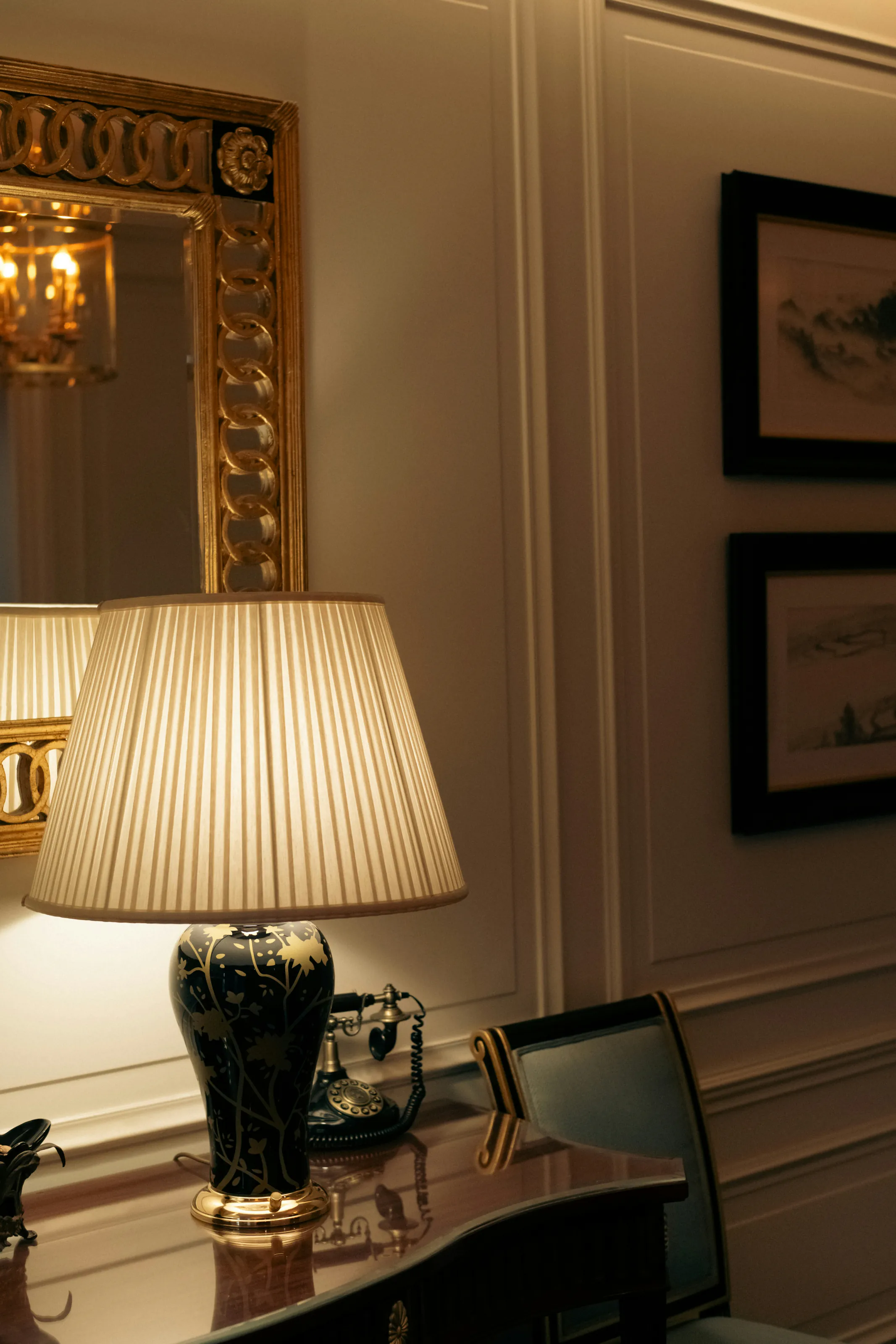 A pleated lamp on a writing desk beneath a gilt mirror
