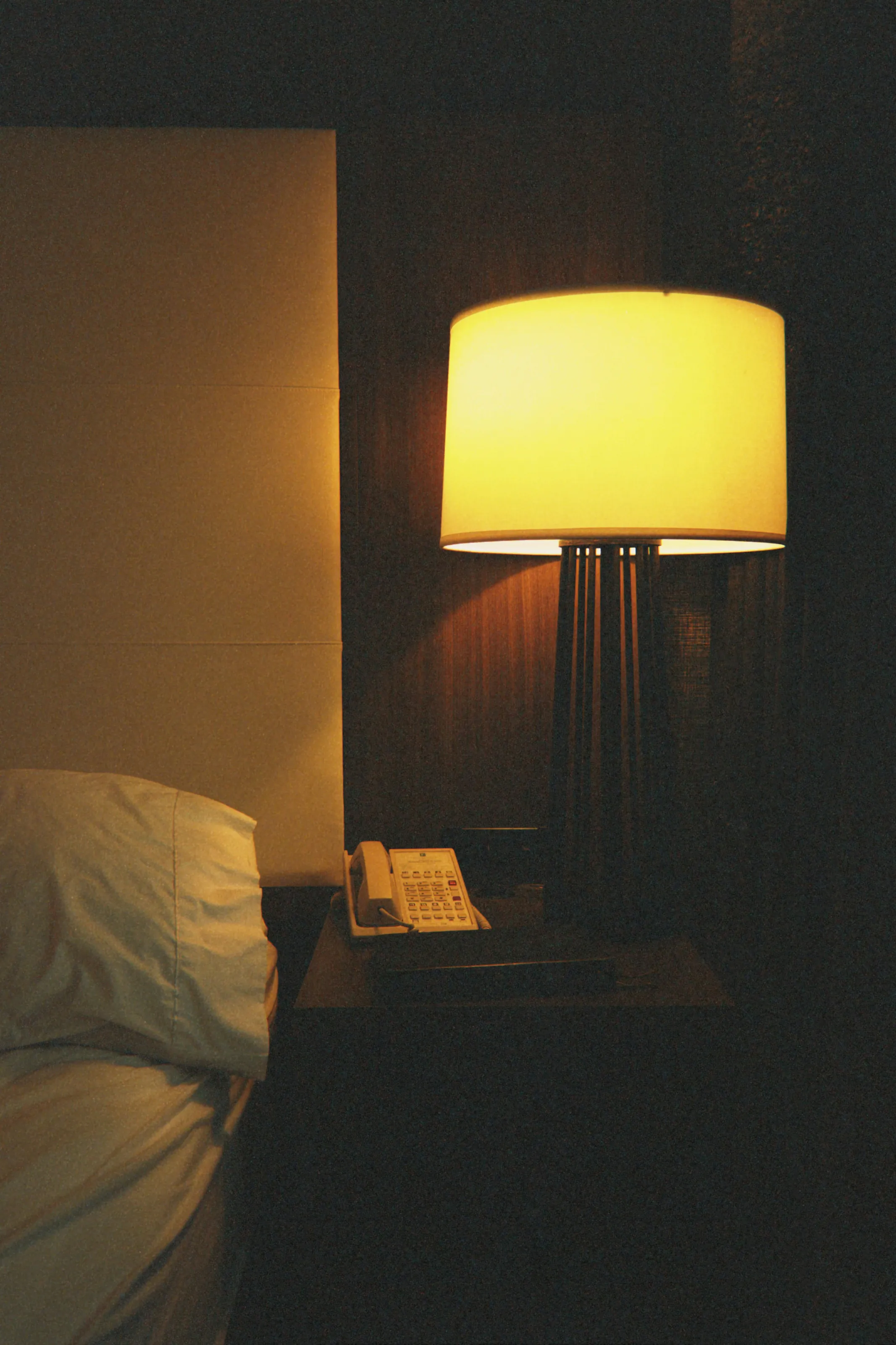 A lamp lit beside the bed in a dark room