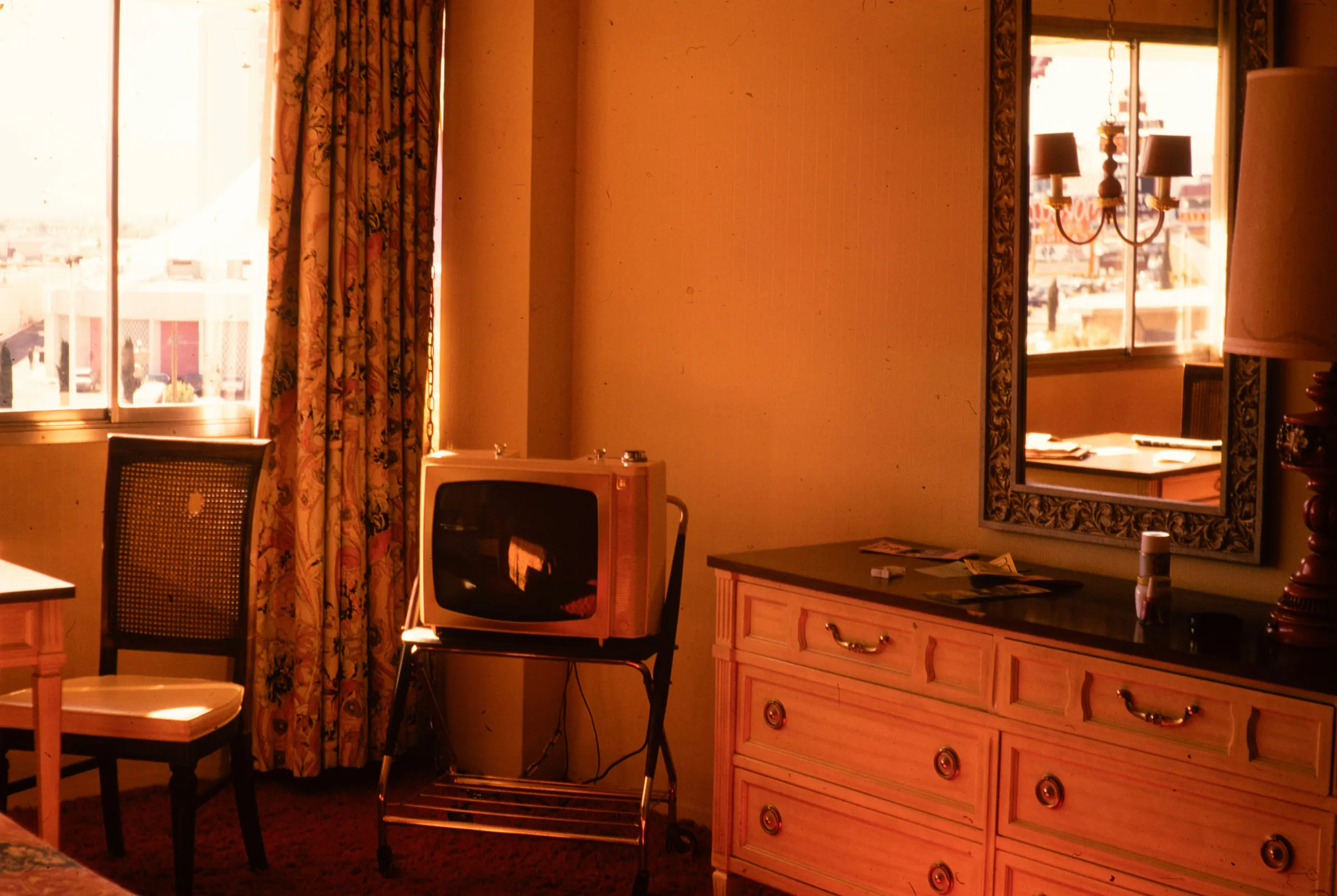 A warm sitting room with a chest of drawers, a mirror and a chair by the window